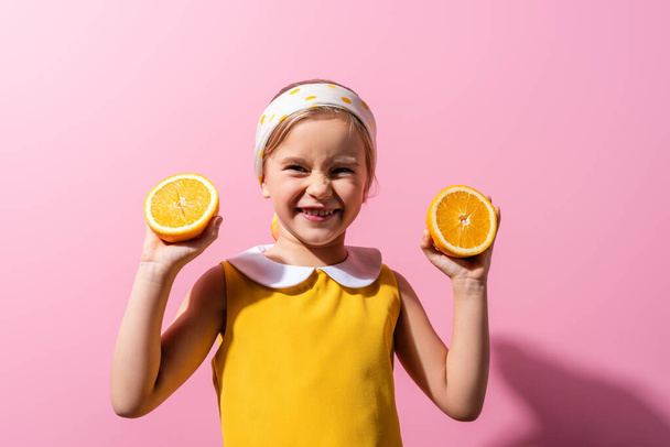 happy girl in headscarf holding orange halves on pink  - Foto, Imagen