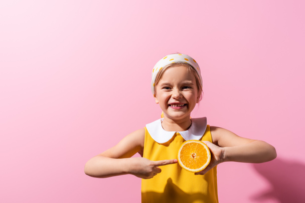 positive girl pointing with finger at orange half on pink - Photo, Image