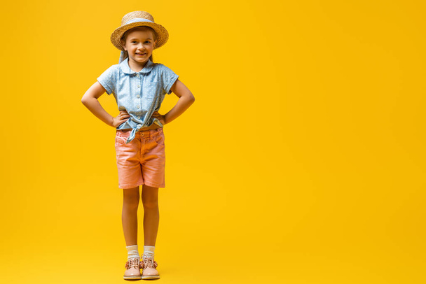 # Hasır şapkalı mutlu bir çocuk # # Elleri sarı kalçalar üzerinde duruyor # - Fotoğraf, Görsel