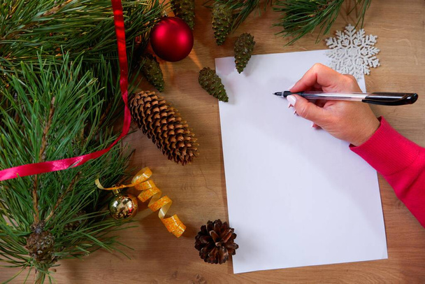 Młoda kobieta pisze kartkę powitalną lub kartkę świąteczną na białym papierze. Boże Narodzenie kulki tło. - Zdjęcie, obraz