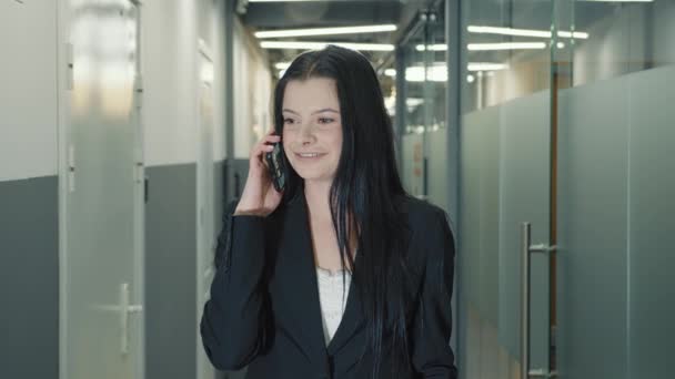 Femme blanche debout dans le couloir du bureau et parlant au téléphone. Femme chef d'entreprise résout cas d'affaires par téléphone mobile. - Séquence, vidéo