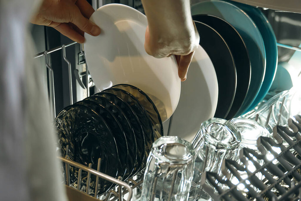 Женские руки вынимают чистую тарелку из открытой посудомоечной машины - Фото, изображение