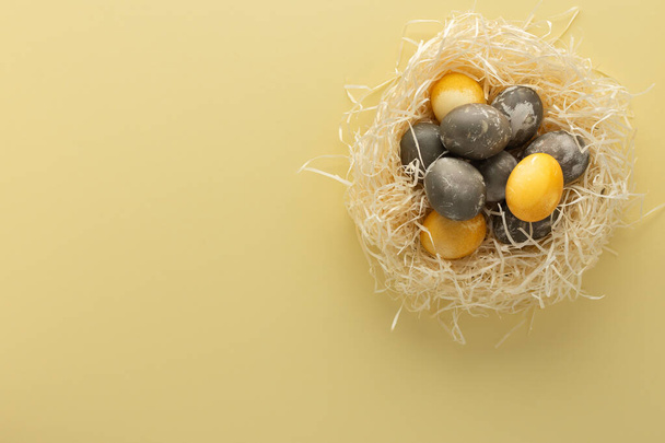 Zlatá a stříbrná velikonoční vejce v slámovém hnízdě, velikonoční hnízdo izolované na žlutém pozadí - Fotografie, Obrázek