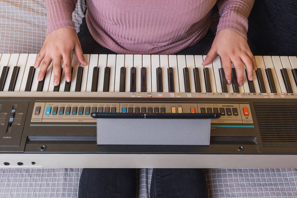 zwei Hände eines jungen Mädchens im lila Pullover, das mit ihrem Tablet Klavier spielt. - Foto, Bild