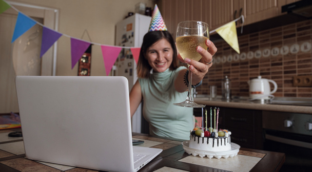 Donna che celebra il suo compleanno attraverso la videochiamata festa virtuale con gli amici. Si accende e spegne la candela. Autentico posto di lavoro a casa decorato. Focolaio di coronavirus 2021. - Foto, immagini