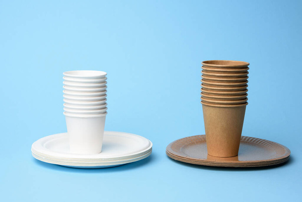 stack of white and brown paper cups and round plates on a blue background, zero waste - Photo, Image