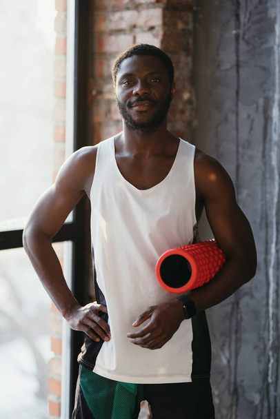 African american man stands in a sports uniform and holds a massage roller in his hands - Foto, imagen