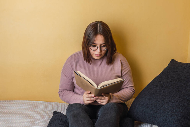 junge lateinische Frau sitzt im Bett und liest ein Buch in ihrem Zimmer in Barcelona, Spanien - Foto, Bild