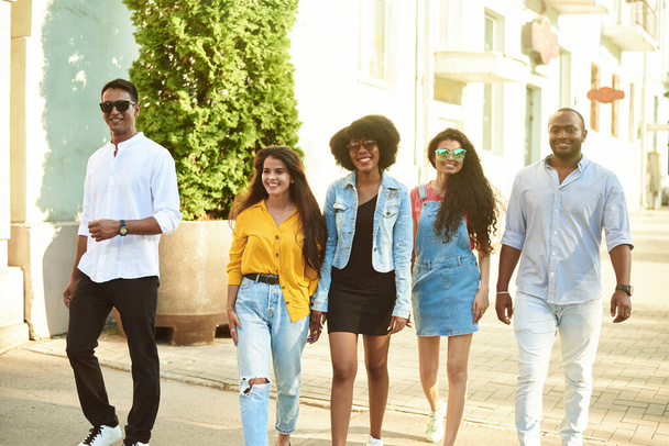 Smiling multiethnic diverse friends speak walking on the street. Communication concept - 写真・画像