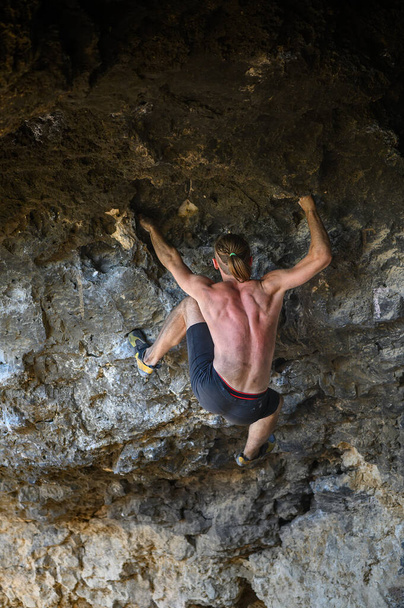 Νεαρός άντρας σκαρφαλώνει σε ένα βράχο σε μια σπηλιά - Φωτογραφία, εικόνα