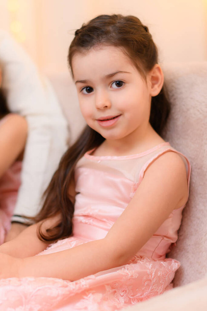 child girl portrait, sitting on a couch in home interior decorated with lights - Photo, Image