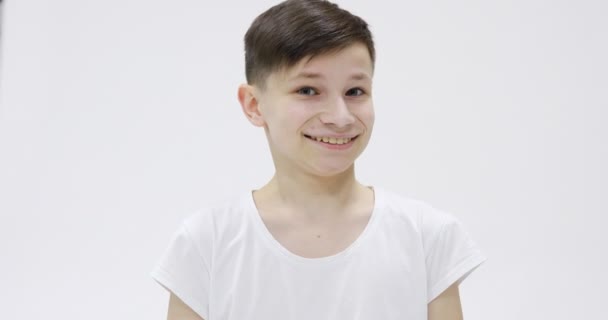 Όμορφος έφηβος 14s σε λευκό t-shirt ευτυχώς χαμογελαστός απομονωμένος πάνω από λευκό φόντο στο στούντιο. Άνθρωποι ειλικρινή συναισθήματα, έννοια του τρόπου ζωής. Κοιτάζοντας την κάμερα με γοητευτικό χαμόγελο, έκπληξη. - Πλάνα, βίντεο