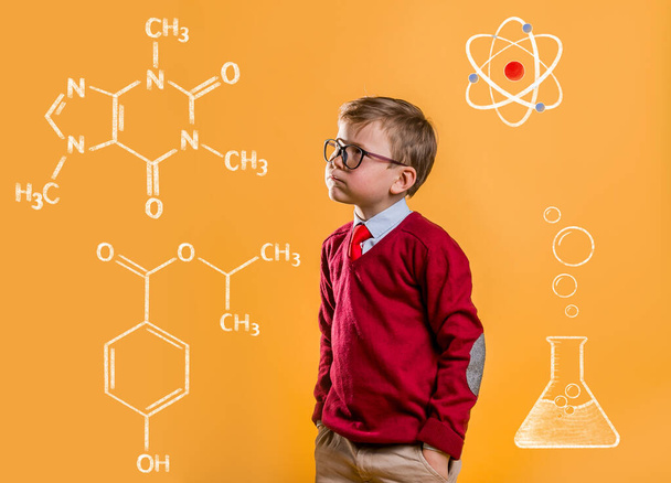 Back to school. Confident schoolboy in big glasses standing by the yellow school wall with chemical formulas on it. Chemistry. Science and education. Success, motivation, winner, genius, innovation. - Photo, image