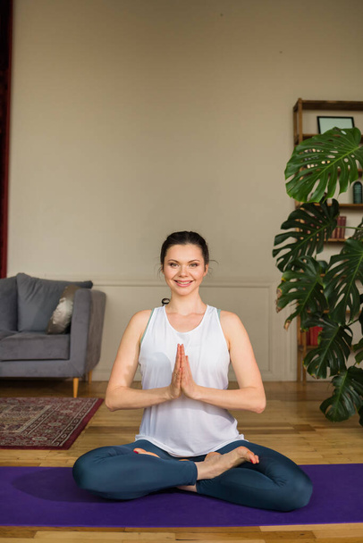 morena en ropa deportiva está practicando Padmasana asana en una habitación. Yoga en casa - Foto, Imagen