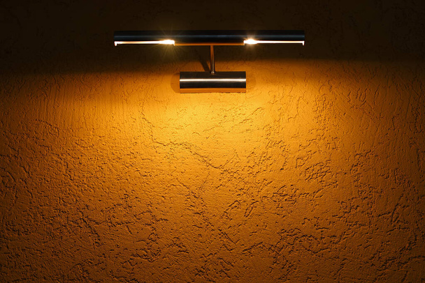 A parede de textura amarela é iluminada por um acessório de luz no topo.  - Foto, Imagem