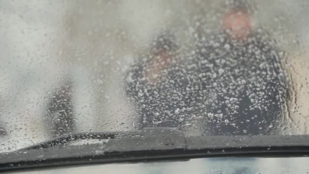 Kaupunkimaiseman siluetit ihmisistä, jotka kävelevät auton tuulilasista pyyhkimillä talvella - Materiaali, video