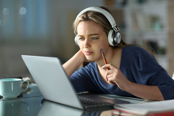 Pensive student wearing wireless headphones e-learning using laptop in the night at home - Fotoğraf, Görsel