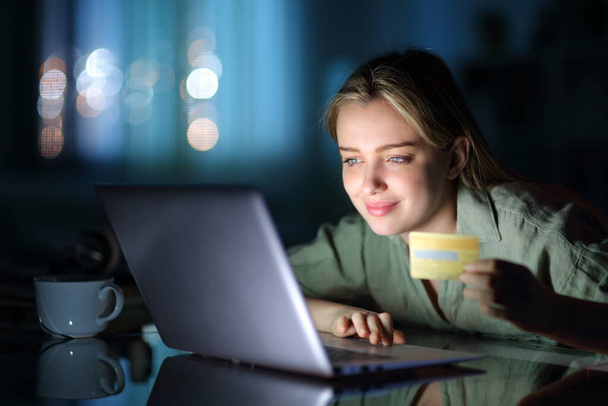Satisfied teen paying with credit card and laptop in the night at home - Photo, image