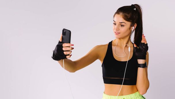 Banner. Caucasian girl in sportswear makes a selfie on a smartphone smiling on a gray background. - Fotoğraf, Görsel