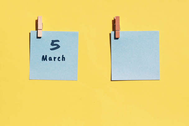 5 Μαρτίου. Ημέρα των 5 μηνών, ημερολογιακή ημερομηνία. Δύο μπλε σεντόνια για γράψιμο σε κίτρινο φόντο. Πάνω όψη, αντίγραφο χώρου. Άνοιξη μήνα, ημέρα του έτους έννοια - Φωτογραφία, εικόνα