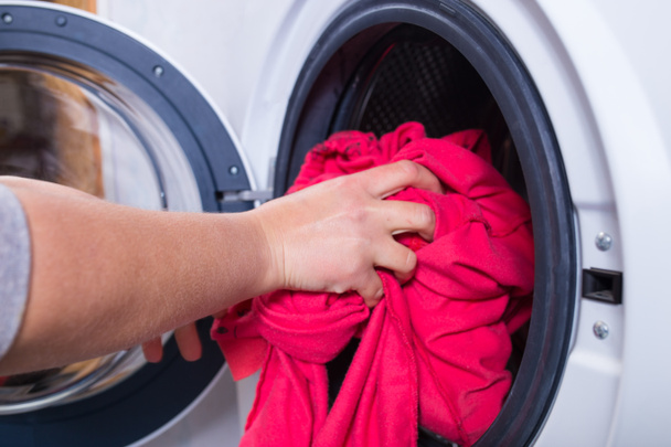 Hand putting pink cloth to the washing mashine close up. - Photo, Image