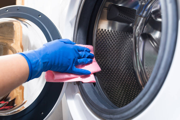 Hand in blue glovesw cleaning washing mashine with piece of cloth - Fotografie, Obrázek