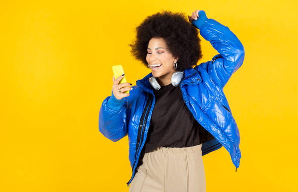 woman talking with smartphone, happy smiling, listening to music and dancing, urban clothes and headphones, copy space - Foto, Imagen