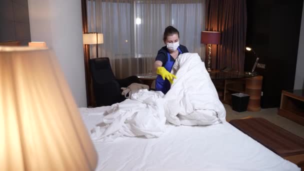 Μασκαρισμένη οικιακή βοηθός αφαιρώντας φαρδιά λινά από το κρεβάτι - Πλάνα, βίντεο