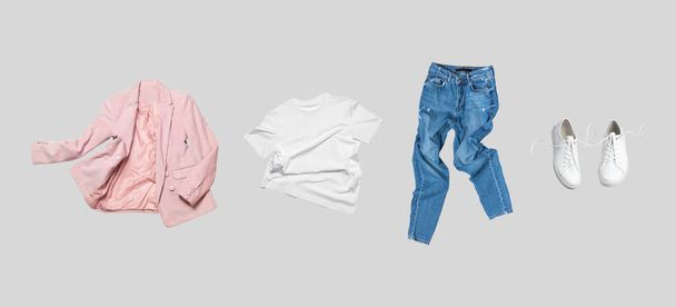 Weißes fliegendes Baumwoll-T-Shirt, blaue Jeans, weiße Lederturnschuhe, modische rosafarbene Blazerjacke auf grauem Hintergrund. Saubere Markenkleidung. Mock up für Ihr Design. Frühling Sommerkleidung. - Foto, Bild