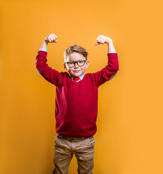 Kids power. Child showing bicep muscles against yellow background. Strong man concept. Stylish pupil of business school. Education power, strength, confidence or defense from bullying - Photo, Image