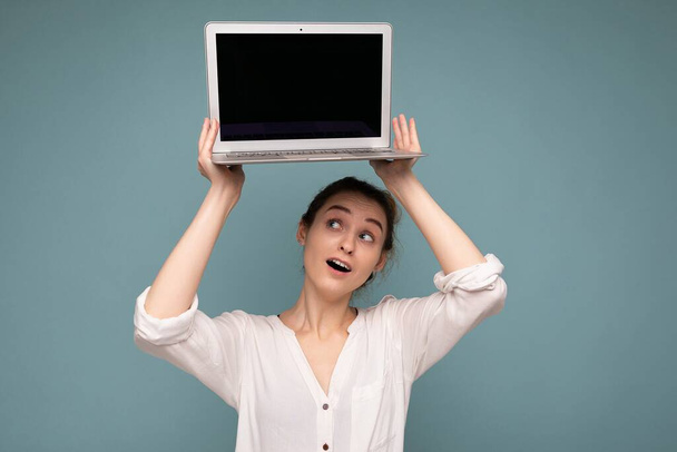 Beautiful smiling happy young woman holding computer laptop looking up at netbook having fun wearing casual smart clothes isolated over wall background - Photo, Image