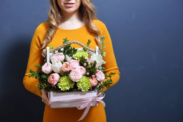 молодая девушка в горчичном платье держит в руках красивую композицию цветов в коробке, созданной флористом. концепция приятной распродажи для отдыха. - Фото, изображение