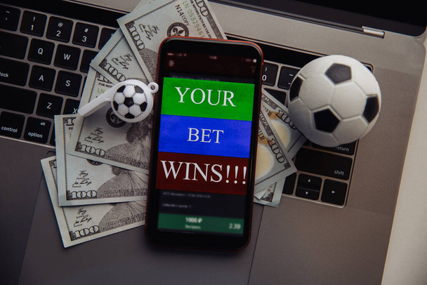 キーボード上のオンラインギャンブルアプリケーション、ドル札やサッカーボールとスマートフォン。賭けの概念。トップ表示 - 写真・画像