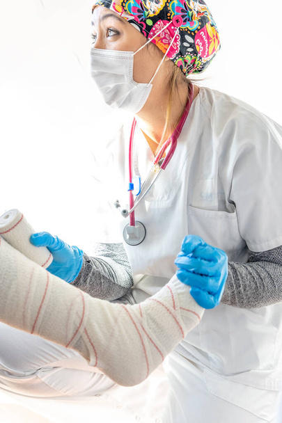 Обрезание медика в латексных перчатках обертывание ноги неузнаваемого пожилого пациента при использовании бинта - Фото, изображение