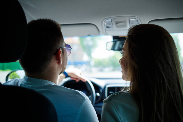 Loving couple in a car hug and hold hands while traveling. Stylish young girl with blond hair of European appearance and a guy in a white polo. Happy relationship concept - Photo, Image