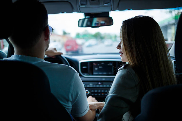 Loving couple in a car hug and hold hands while traveling. Stylish young girl with blond hair of European appearance and a guy in a white polo. Happy relationship concept - Foto, Bild
