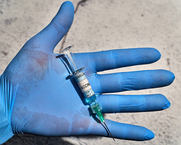 Elinde mavi lateks eldiven ve etiketinde "covid 19 aşı sadece enjeksiyon" yazan bir şırınga var. - Fotoğraf, Görsel