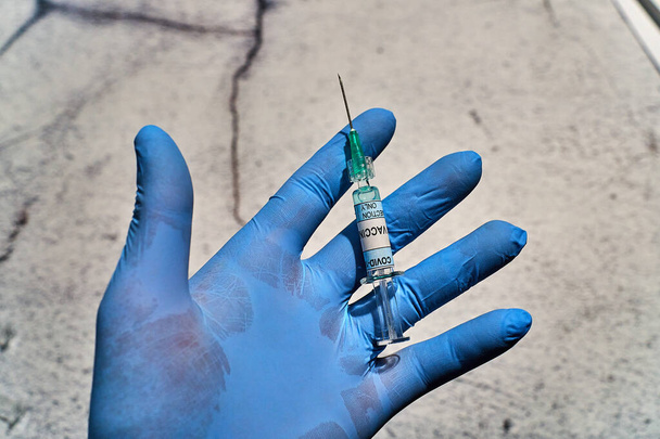 hand with a blue latex glove and a syringe in horizontal position that has written "covid 19 vaccine only injection" on the label - Photo, Image