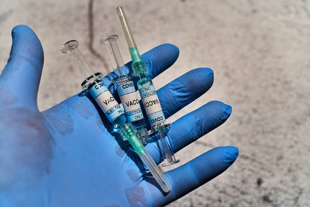 Hand mit blauem Latex-Handschuh und drei Spritzen in vertikaler Position, auf dem Etikett steht "covid 19 impfstoff only injection" - Foto, Bild