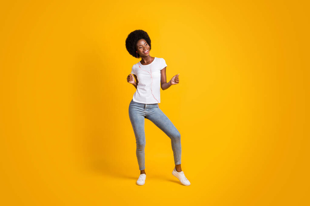 Full length body size photo of smiling girl with black skin listening music dancing keeping hands up isolated on bright yellow color background - Foto, immagini