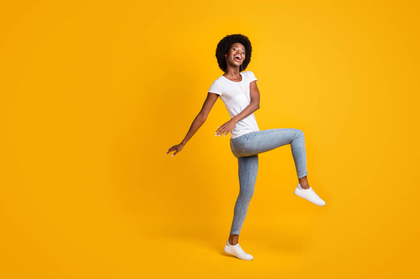 Full length body size photo of positive young woman with black skin listening song dancing with orange earphones isolated on bright yellow color background with empty space - 写真・画像
