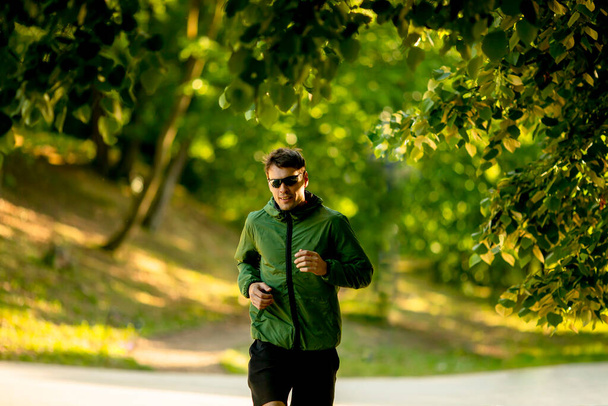 Komea urheilullinen nuori mies käynnissä, kun teet harjoituksen aurinkoisessa vihreässä puistossa - Valokuva, kuva