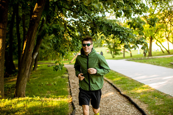 Fešák atletický mladý muž běží při cvičení v slunném zeleném parku - Fotografie, Obrázek