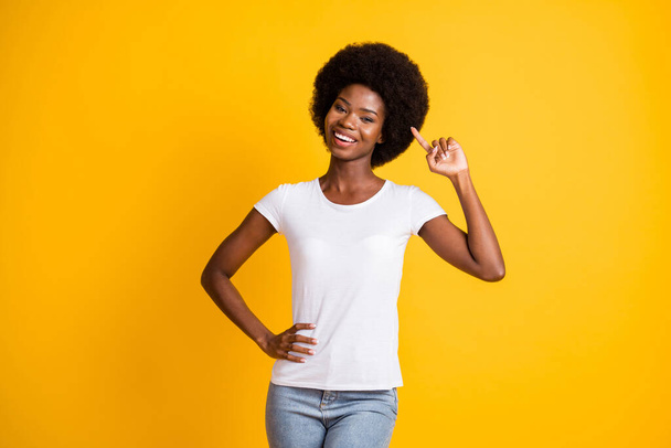 Photo portrait of young african american girl point finger at her afro hair smiling one hand on waist wearing white t-shirt isolated on vivid yellow colored background - Фото, зображення