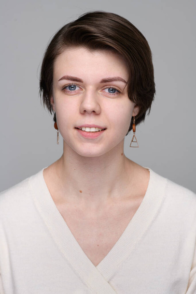 Una ragazza sorridente con gli occhi azzurri e taglio di capelli corto in un gardigan bianco - Foto, immagini