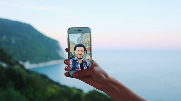 Χέρι κρατώντας smartphone κατά τη διάρκεια της βιντεοκλήσης με τον άνθρωπο μπροστά από τη θάλασσα - Φωτογραφία, εικόνα