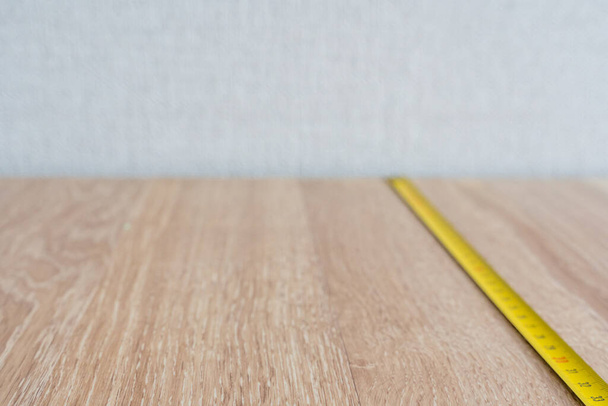 Mesurer le plancher en bois avec bande de mesure jaune, fond abstrait - Concept de reconstruction et de projection hors foyer - Photo, image