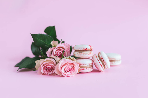 Smaczne francuskie makaroniki z różowymi różami na różowym pastelowym tle. Miejsce na tekst. - Zdjęcie, obraz