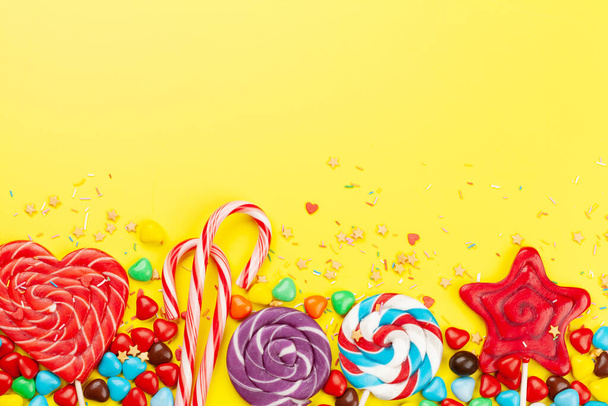 Various sweets assortment. Candy, bonbon and macaroons on yellow background. Top view flat lay with copy space - 写真・画像