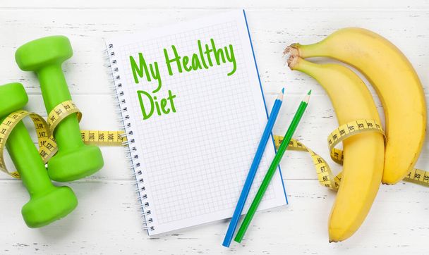 Fitness und gesundes Essen. Hanteln, Obst und Notizblock mit Diät auf Holztisch. Draufsicht flach gelegt - Foto, Bild